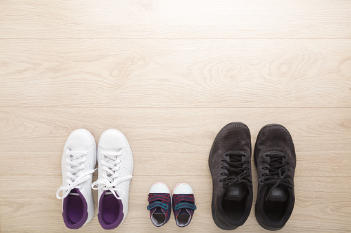 Father, mother and little kid sport shoes on wooden floor background. New family. Closeup. White female, black male and blue baby footwear. Empty place for text. Top down view.