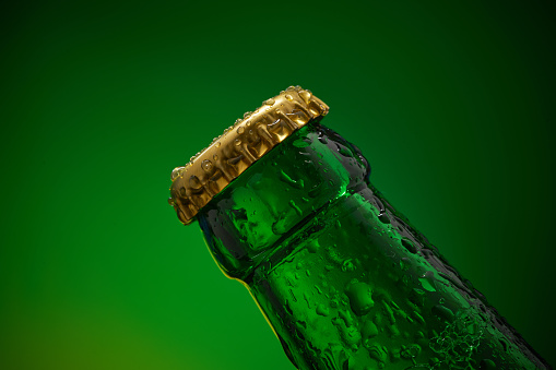 The part of green cold bottle with water drops and golden cap, green background. High resolution, high post-production quality.