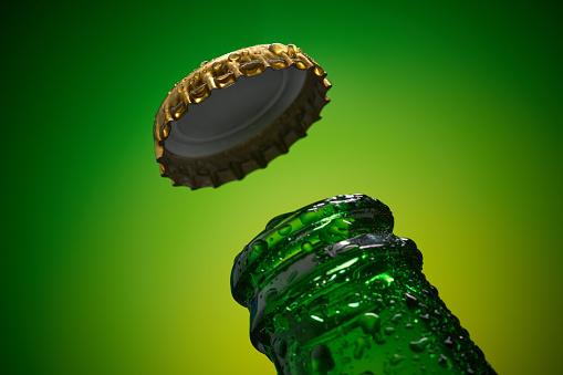 Green cold beer bottle with water drops and golden cap opened on green background. high resolution, high post-production quality.