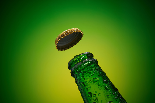 Green cold bottleneck with drops and golden cap opened on green background. high resolution, high post-production quality.