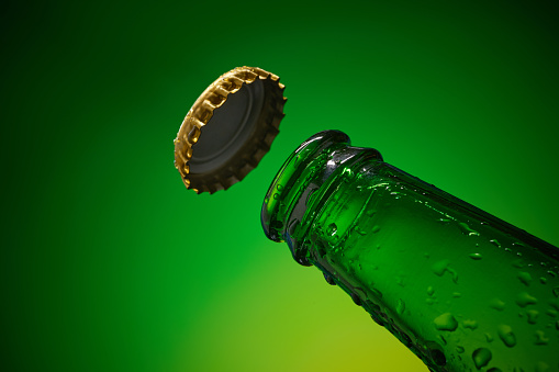 Green cold beer bottleneck with water drops and golden cap opened on yellow green background. high resolution, high post-production quality.
