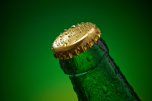 Green cold bottle with water drops and golden cap on green background. High resolution, high post-production quality.