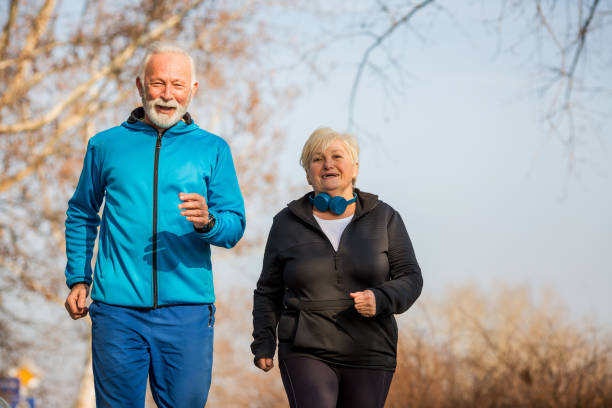 Active seniors jogging. Sunny day in park. Senior couple is jogging, smiling and enjoying in beautiful sunny day. They were exerting and doing warming up exercises and now they are jogging and smiling, pleased by lovely day. aerobics stock pictures, royalty-free photos & images