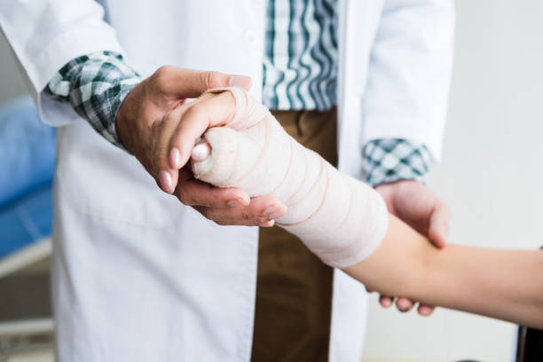 primo piano dell'uomo medico di controllo stecchetta il braccio della mano paziente femminile a causa di con il braccio rotto per una migliore guarigione con un sorriso sedersi su una sedia a rotelle nello sfondo dell'ospedale della stanza. - ingessatura foto e immagini stock