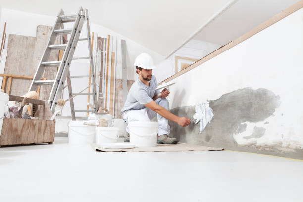 istock man plasterer construction worker at work, takes plaster from bucket and puts it on trowel to plaster the wall, wears helmet inside the building site of a house 1300640639