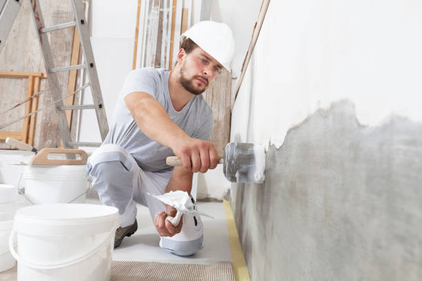 mann gipser bauarbeiter bei der arbeit, nimmt gips aus eimer und legt es auf kelle, um die wand zu verputzen, trägt helm in der baustelle eines hauses - plasterer construction site manual worker plaster stock-fotos und bilder