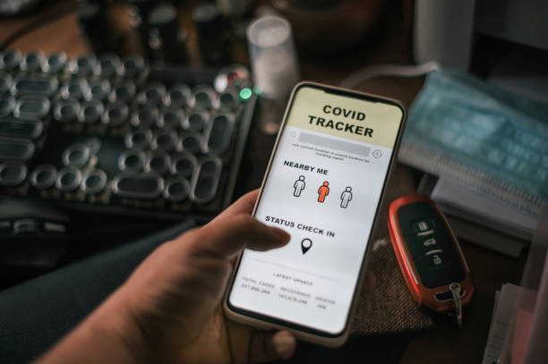 istock a hand holding mobile phone with mobile app Covid-19 contact tracker checking nearby status on number of affected cases with surgical face mask, hand sanitizer, keyboard, car keys, wallet  on table 1300640735