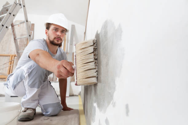 istock construction worker painter man with protective helmet, brush in hand restores and paint the wall, inside the building site of a house, closeup 1300640786