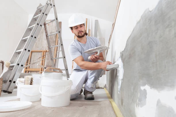 istock man plasterer construction worker at work, takes plaster from bucket and puts it on trowel to plaster the wall, wears helmet inside the building site of a house 1300640799
