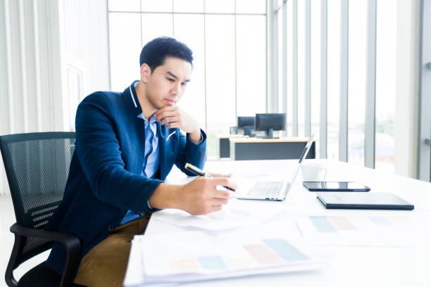 istock asian young businessman have ideas make a note business plan of notebook and laptop computer on wooden table background in office. 1300643583