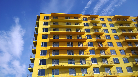 Facade of new multi-story residential building. Blue sky background. House Share. Real estate investing. Buy, sale, rental and insurance apartment in crisis. Housing development. Illuminating yellow.