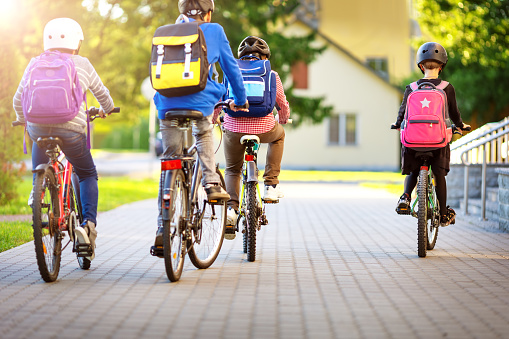 Niños con mochilas montando en bicicleta en el parque cerca de la escuela photo