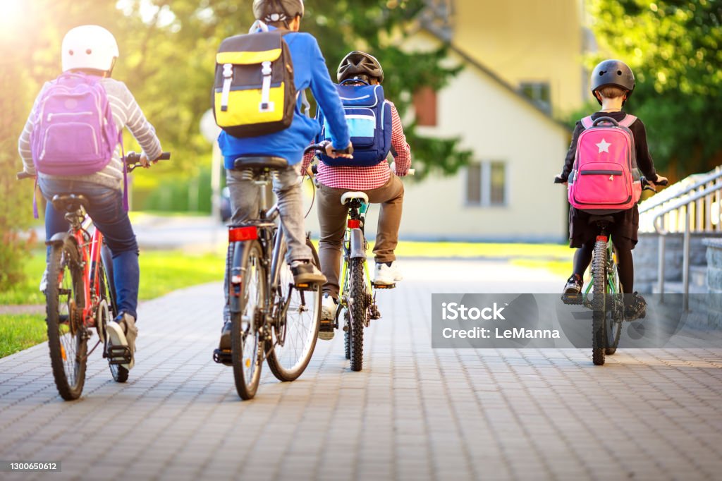 Children with rucksacks riding on bikes in the park near school Children with rucksacks riding on bikes in the park near school. Pupils with backpacks outdoors Cycling Stock Photo