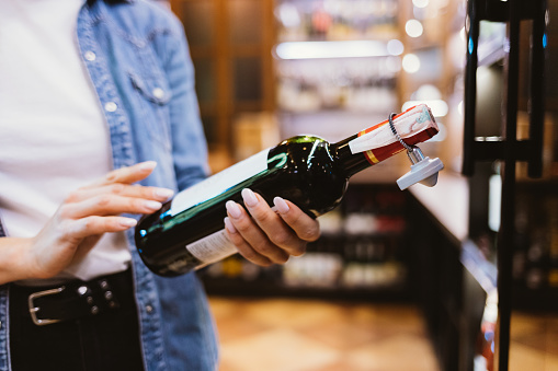 Close-up female hands holding bottle of wine in supermarket.