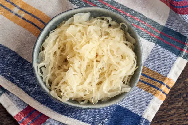 Fermented cabbage in a bowl on a colorful dish towel, top view