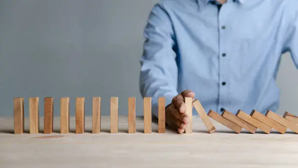 Businessman hand stopping the domino wooden effect concept for Planning,risk and strategy in business.