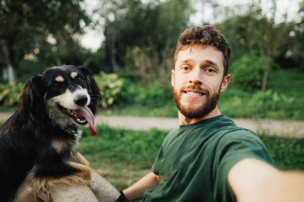 istock Young man is playing with a dog and do selfie 1300658120