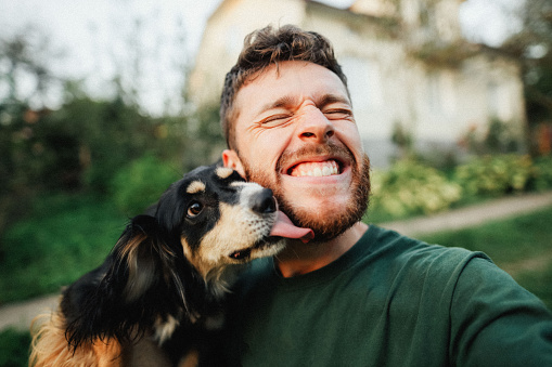 Selfie of a young handsome man with his dog on the green yard in the countryside at the sunset on summer