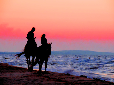 Black silhouettes in the twilight sunset light of horses and a girl with a man riders on the seashore, romantic date, couple in love