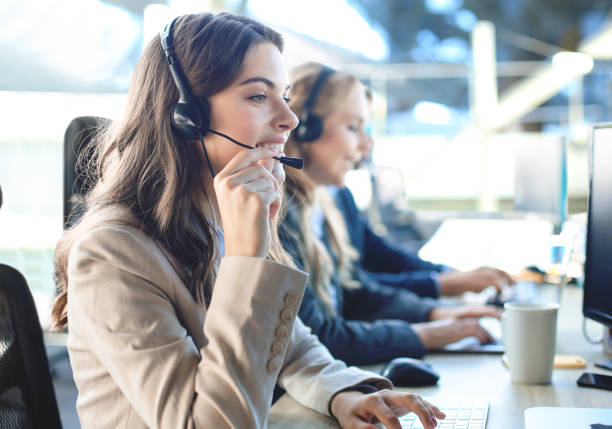 istock Female customer support operator with headset and smiling, with collegues at background. 1300661142