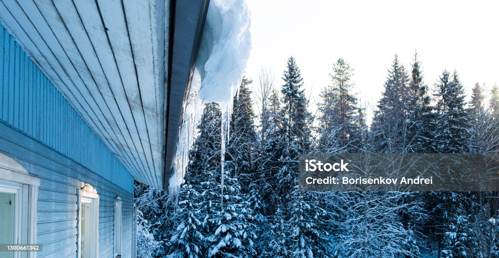 Snow and icicles on the roof of a wooden house. Spring season. House Stock Photo