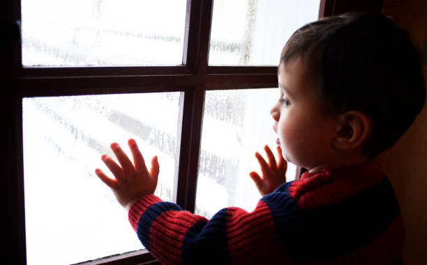 istock A little boy puts his hands on the panes of a window 1300665553