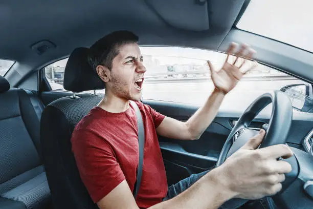 Photo of Angry man driver reacts aggressively to other road users. Concept of psychological problems, anger, and traffic accidents