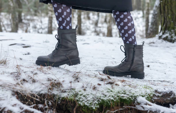 istock Female boots on snowy path, side view. Legs walking or strolling in winter forest in funny cute tights with hearts print for 14 February 1300667718