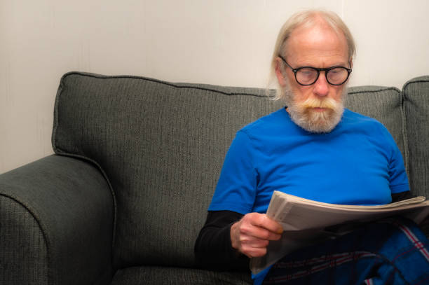 istock Senior man relaxing on a sofa while he reads a newspaper in his own home 1300672818