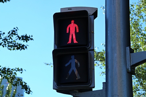 Close-up of red traffic light for pedestrians with a blue sky in the background.