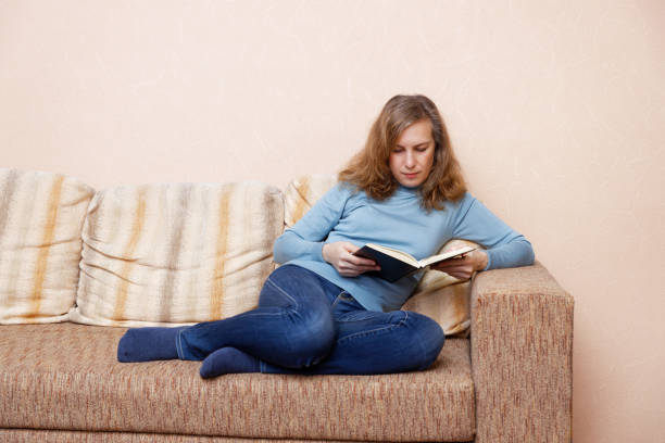 istock Woman sitting at home on the sofa and reading a book 1300685171