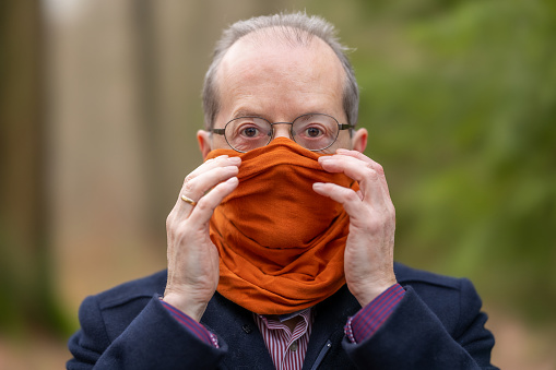Middle aged man outdoors in the forest, nature, wearing a neck gaiter, bandana type of face protection mask against Coronavirus, COVID-19