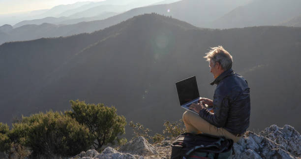 istock Mature man uses computer on mountain top at dawn 1300689695