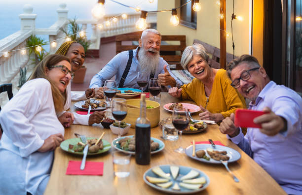 행복한 다민족 선배 친구들이 집 안뜰에서 모바일 스마트 폰으로 셀카를 찍으면서 함께 즐거운 식사를하는 행복한 다인종 선배 - 노인 라이프 스타일 사람들과 음식 개념 - senior adult friendship group of people restaurant 뉴스 사진 이미지