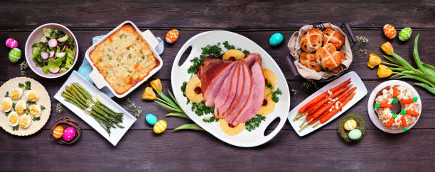 istock Classic Easter ham dinner. Top view table scene on a dark wood banner background. 1300698739