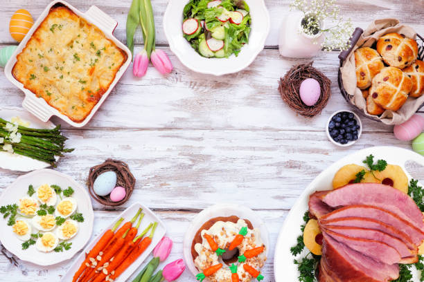 Classic Easter ham dinner. Above view frame on a white wood background with copy space. Classic Easter ham dinner. Above view frame on a white wood background with copy space. Ham, scalloped potatoes, vegetables, eggs, hot cross buns and carrot cake. april photos stock pictures, royalty-free photos & images
