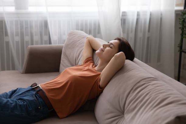 istock Calm young female reclining on sofa with hands behind head 1300701432