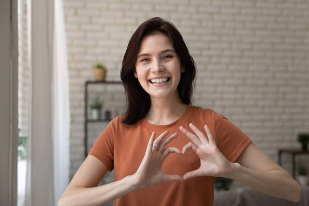 istock Romantic young lady looking at camera uniting fingers in heart 1300701439