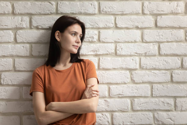 Confident millennial female with light smile standing near brick wall