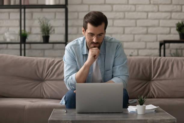 istock Pensive young male working at home focused on computer screen 1300701487