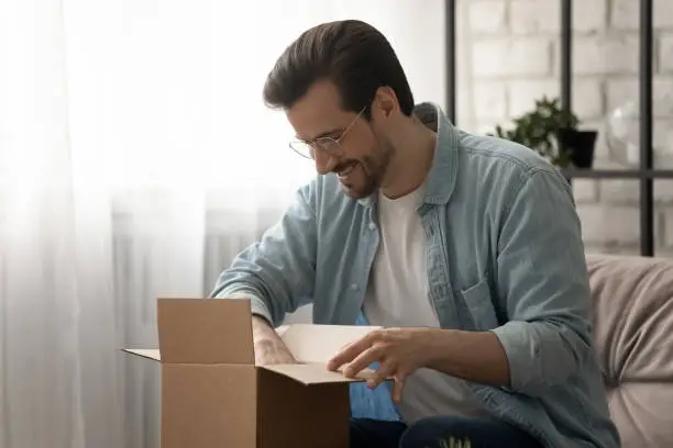 Photo of Young man loyal client of postal service unboxing small package