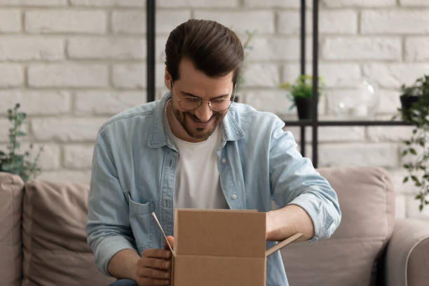 istock Curious millennial male sitting on couch at home opening parcel 1300701512