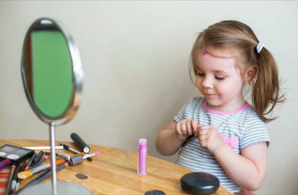 istock Adorable little child playing with cosmetics and doing makeup while looking in mirror 1300703247