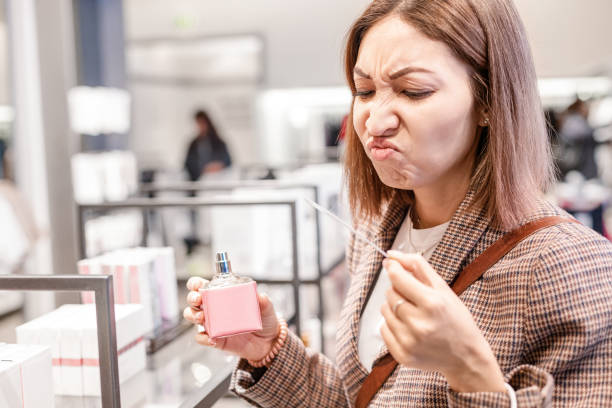 la femme asiatique renifle le parfum avec un parfum dégoûtant et terrible. concept de mauvais goût et perte d’odorat - asian ethnicity women shopping mall perfume photos et images de collection