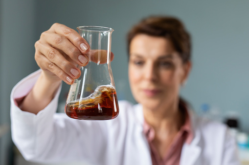 Woman scientist closely observing a brown liquid in a chemical flask.