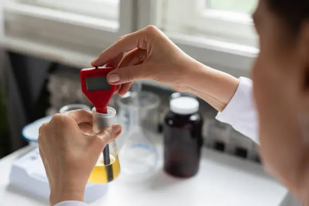 Researcher using a lab instrument to measure the pH value of a solution in a chemical flask, a close up.