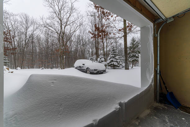 A car covered by snow under snowfall. Looking from the inside of the garage.