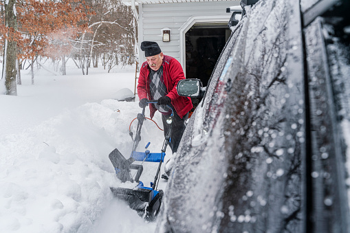 Senior retired Caucasian White man cleaning the snow around his home after the winter snowstorm.