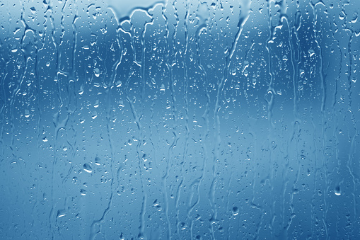 Water droplets on glass in front of a blue background.