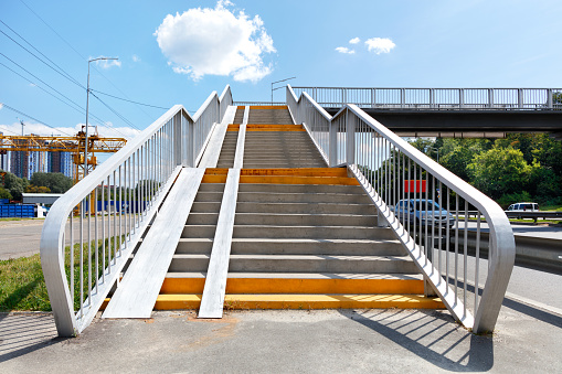 A staircase going up to a pedestrian bridge, an overpass and a crossing over a high-speed highway on a bright sunny day against the backdrop of a blue sky with a cloud. Copy space.